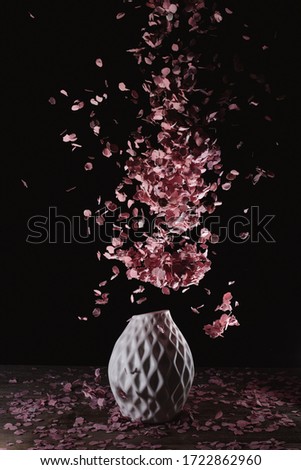 A white vase with black background seems to errupt pink confetti