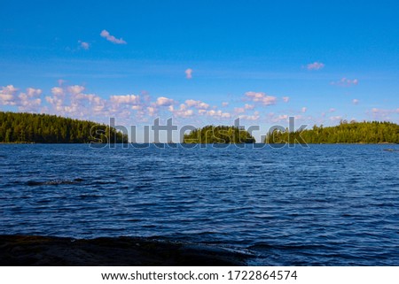 Calm lake with islands in the water, green forest on the islands. Clear, blue sky with white clouds in Karelia, horizontal photo, vacation concept.