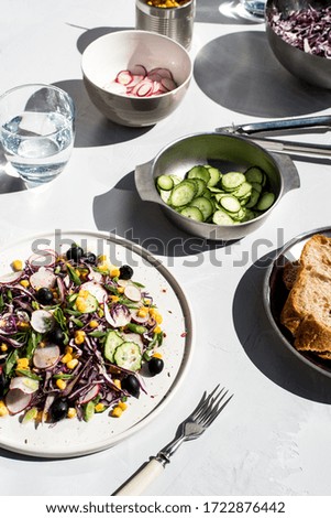 Photo of a fresh spring salad on a white porcelain plate and vegetable mix of ingredients in metal bowl on a white rustic background sunlight with shadows