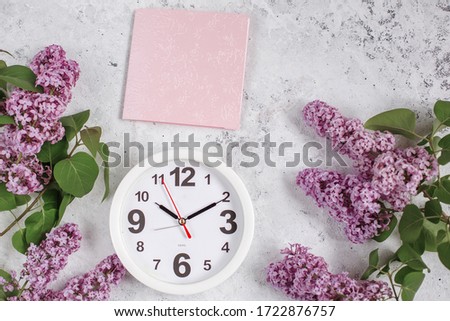 a branch of lilac and a pink card, a clock lying on a gray background