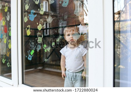 A boy paints with palms on the window. Quarantine