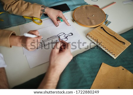 Close-up of two fashion designers drawing sketch of new dress with pencils together