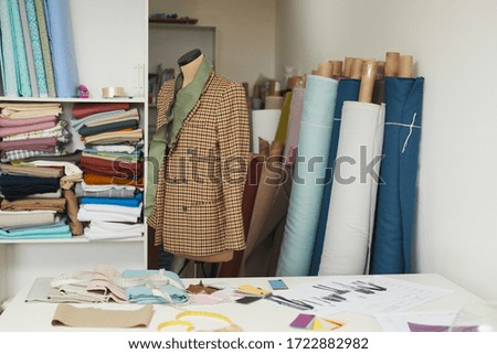 Image of model of stylish jacket on mannequin in the workshop with fabric rolls in the background