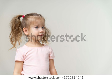 a beautiful girl of 3-4 years old stands against a white wall and smiles cute. copy space