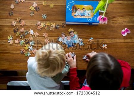 Two children, boys, assembling puzzle with their picture from an autumn forest, playing at home together