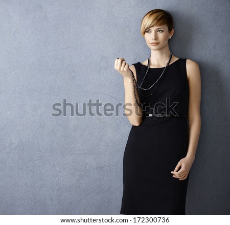 Attractive young woman wearing black dress and pearl necklace on grey background