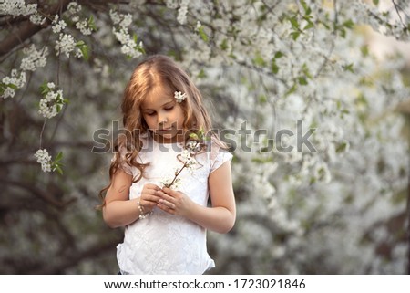 A long-haired girl stands in a blooming garden, holding a sprig of flowers. An image with selective focus and toning.