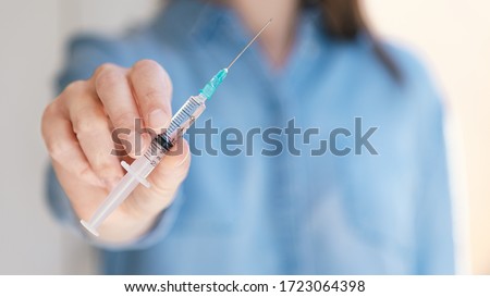 Woman holding medical injection syringe in her outstretched hand towards the camera. Selective focus, copy space Royalty-Free Stock Photo #1723064398