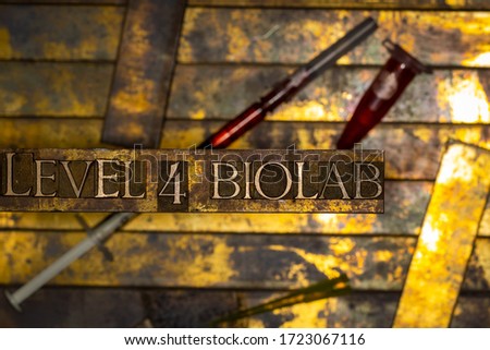 Photo of real authentic typeset letters forming Level Four Biolab text with syringe and test tube on vintage textured grunge copper and gold background