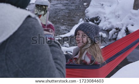 Girl smiling for photo as she sits in hammock outside in the snow during winter as her sister takes pictures.