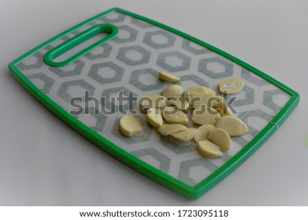 Closeup top down view of a fresh uncooked garlic slices which are laying on cutting board with checkered green pattern