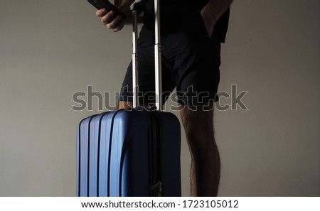 Man holding phone waiting with travel suitcase