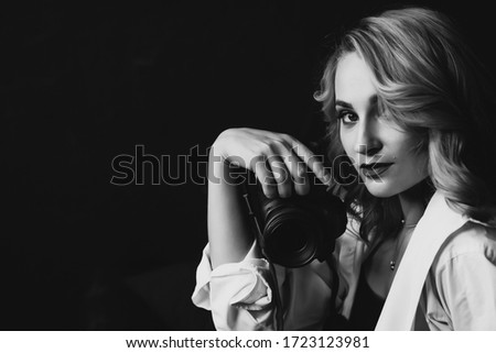 Portrait of a beautiful woman photographer with a camera in her hands in low key. Black and white art photo. Soft selective focus.