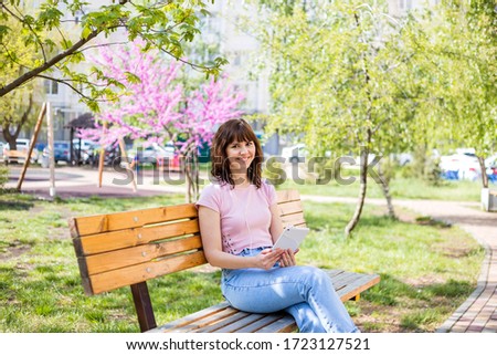 A young girl sits on a bench in the Park and looks at a tablet. Distance learning in quarantine.