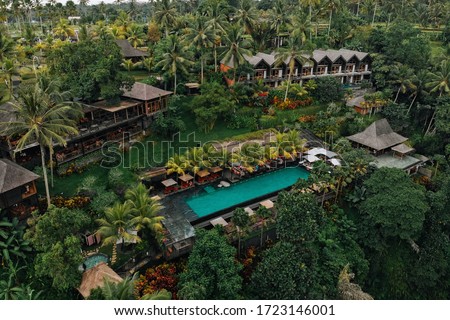 Aerial view of luxury hotel with straw roof villas and pools in tropical jungle and palm trees. Luxurious villa, pavilion in forest, Ubud, Bali Royalty-Free Stock Photo #1723146001