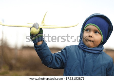 Seriously kid playing with toy airplane against white summer sky background.