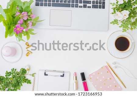 Flat lay blogger or freelancer workspace with a laptop, cup of coffee, small flowers and green leaves, office supplies on a light background