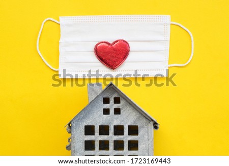 Sweet home concept, mini house, surgical mask and red heart on yellow background, top view, flat layout