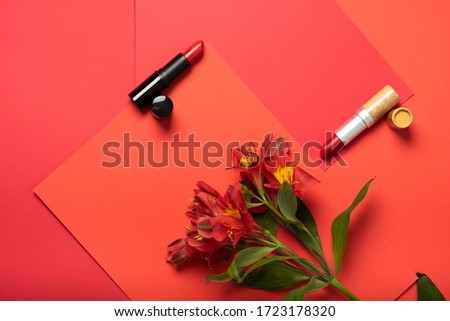 Creative geometric composition of red lipsticks lying on a red craft paper and red flowers bouquet. Beauty and make up, present for girl. Top view Royalty-Free Stock Photo #1723178320