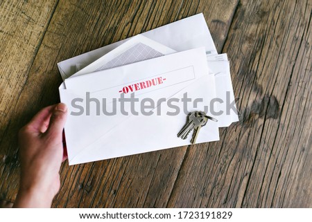 Hands of a woman hold an letter with that reads Overdue in an envelope - Keys - Table - Late Payment Royalty-Free Stock Photo #1723191829