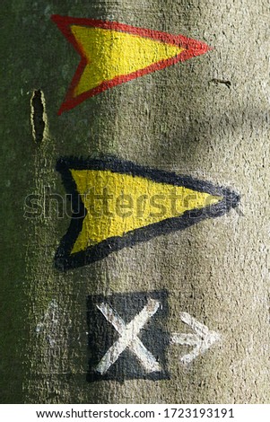 Three signposts on a tree. Two yellow arrows and one black x.