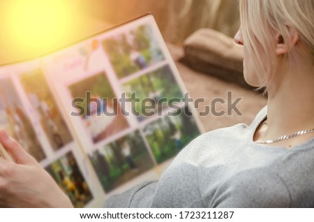 girl in a gray jacket is sitting on the sofa and looking at old photos in a photo album
