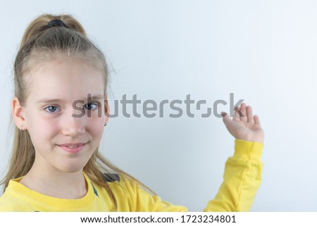 Workpiece or template with beautiful, nice, cool and pretty young girl or child in yellow T-shirt on white showing domonstrating something behind her on background by means of her hand as presentation