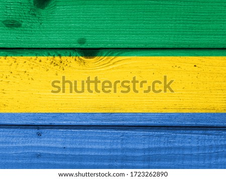 Gabon flag painted on old wood plank background. Brushed natural light knotted wooden board texture. Wooden texture background flag of Gabon