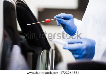 Medical worker wearing personal PPE surgical gloves and protective clothing,holding nasal swab,performing drive-thru COVID-19 testing,point of care on site location for PCR detection of Coronavirus  Royalty-Free Stock Photo #1723264381