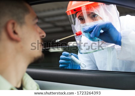 Medical NHS UK worker performing drive-thru COVID-19 check,taking nasal swab specimen sample from male patient through car window,PCR diagnostic for Coronavirus presence,doctor in PPE holding test kit Royalty-Free Stock Photo #1723264393