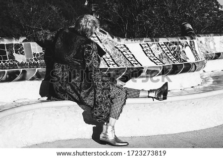 Compatibility, elderly wellbeing concepts. Barcelona, Spain. Senior stylish lady (unrecognizable; back view) relaxing on mosaic bench in Guell park. Catalonia travel background. Black white photo.