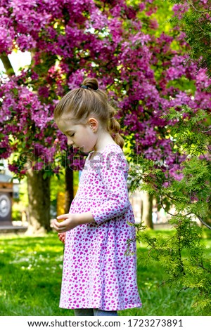 beautiful little girl in a dress possing near a flowering tree with pink blooms
