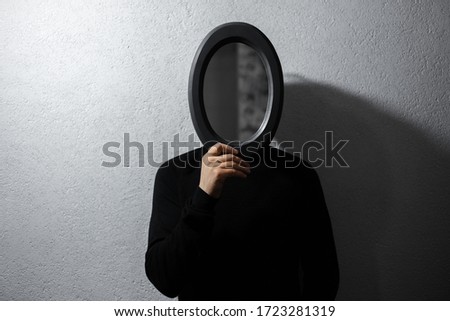 Dramatic portrait of man with black mirror on face. Background of white textured wall. Royalty-Free Stock Photo #1723281319