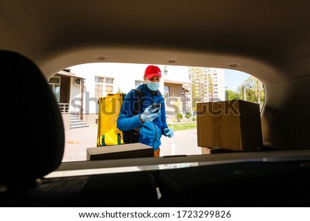 food delivery man in a protective mask and gloves with a thermo backpack near a car during the quarantine period