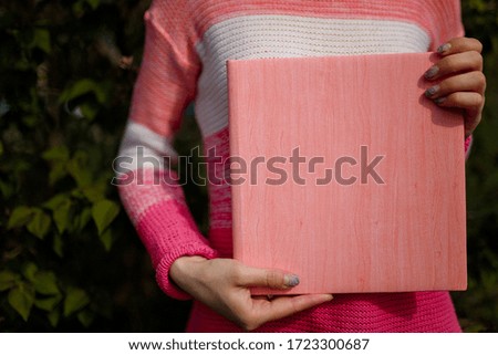 Female hands holding photobook or photoalbum with leather pink cover and wooden texture.