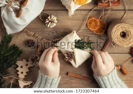 Zero waste and eco friendly christmas concept. Female hands wrap gifts in natural fabric with ornaments made of natural materials, top view, flat lay Royalty-Free Stock Photo #1723307464