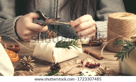 Zero waste and eco friendly christmas concept. Female hands wrap gifts in natural fabric with ornaments made of natural materials