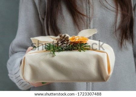 Zero waste and eco friendly christmas concept. Young woman holding in her hands a gift wrapped in natural fabric and decorated with natural materials