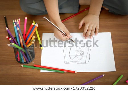A child little boy hand with color pencil is drawing a house.