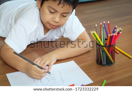 Cute little boy drawing a house with color pencils.