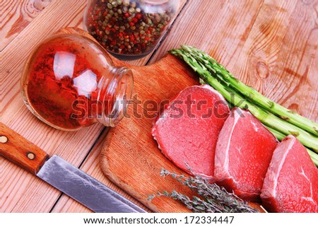 prime fillet meat : dry raw beef on cutting board with asparagus , thyme bundle , color peppercorn mix and red paprika powder mixed with dry spices over wooden table ready to cooking