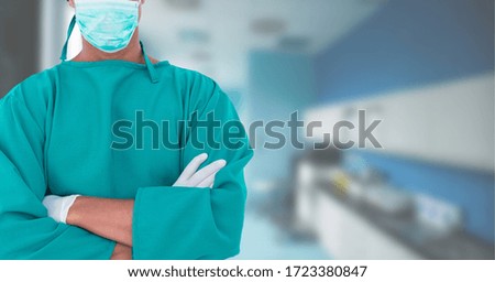 Mid section of male doctor wearing surgical gloves and protective face mask against coronavirus Covid-19 and scrubs standing with arms crossed working in a hospital. Medicine public health pandemic