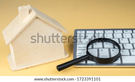 Hand holding a magnifying glass over a home model.
Finding a house. Search for housing. 
