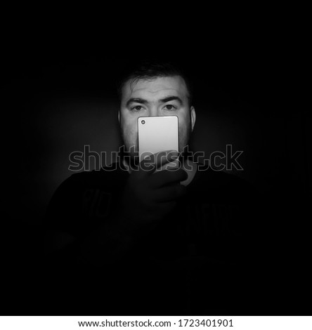 handsome middle age  man looking at far away with mobile phone surprisedly with black shirt  in front of black background. white cell phone. studio shot