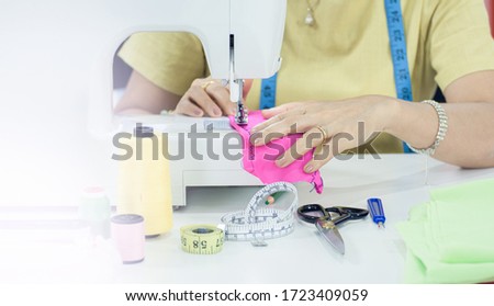 Focus on hands using sewing machine to make dress with blur foreground on the left side for copy space.