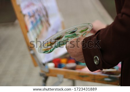 Woman artist paints in a park on an easel. Colored pictures of paints, aesel and tassels