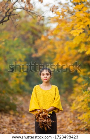 smiling girl plays with yellow maple leaves in autumn in the forest