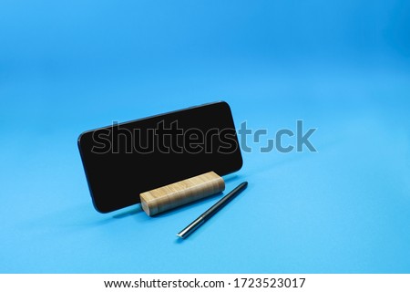 View of a smart phone on the desk holder with an electronic pen isolated on blue background.  Information and technology concept
