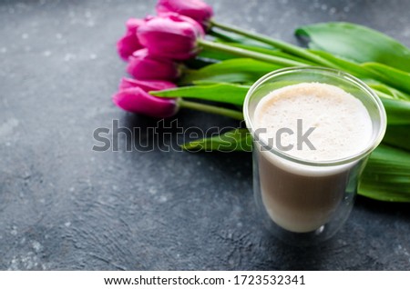 Cup of coffee with foam and bouquet of pink tulips on black background. Breakfast on Mothers day, Valentines Day or Womens day. Romantic morning concept. Copy space.