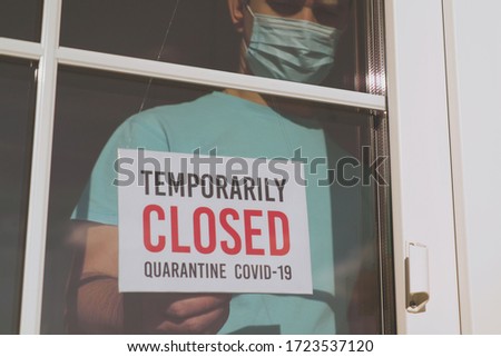 Small business sign on the storefront window closed because of coronavirus or COVID19. Business owner in medical mask puts a CLOSED sign on the front door due to the coronavirus COVID19 pandemic.
